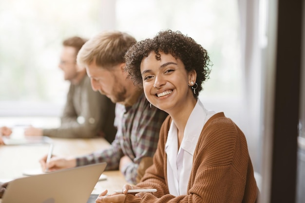 Glimlachende jonge vrouw zittend aan een tafel in een coworking-centrum