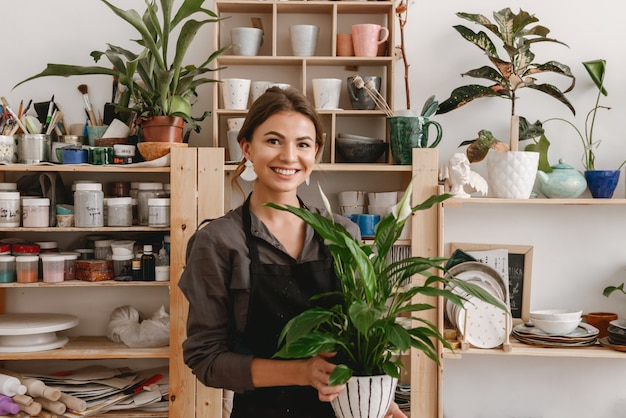 Glimlachende jonge vrouwelijke keramist bedrijf plant.