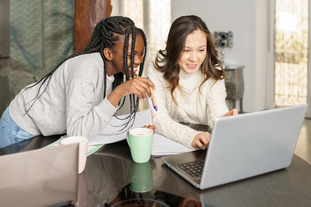 Glimlachende jonge vrouwen die thuis aan een laptop werken.
