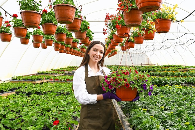 Glimlachende jonge vrouwenbloemist die een pot petunia's in serre houdt Vrouwelijke tuinman die met installaties werkt