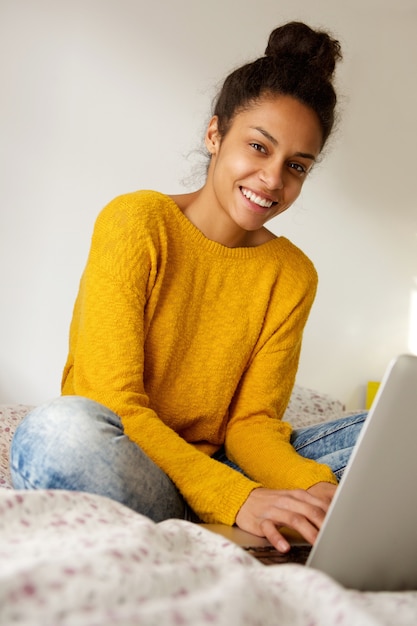 Glimlachende jonge vrouwenzitting op bed met laptop