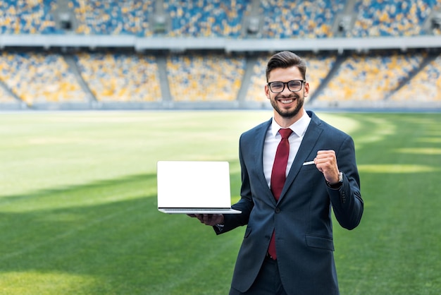 Glimlachende jonge zakenman in pak die een ja-gebaar toont terwijl hij een laptop vasthoudt met een leeg scherm