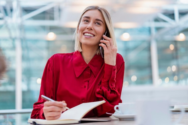 Glimlachende jonge zakenvrouw met notitieboekje aan de telefoon