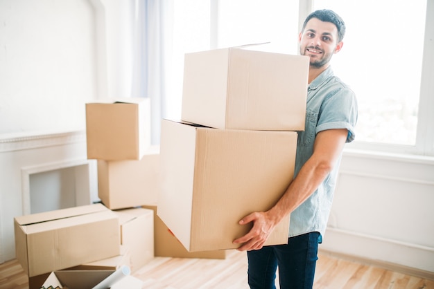 Glimlachende jongeman houdt kartonnen dozen in handen, housewarming. Verhuizen naar een nieuw huis