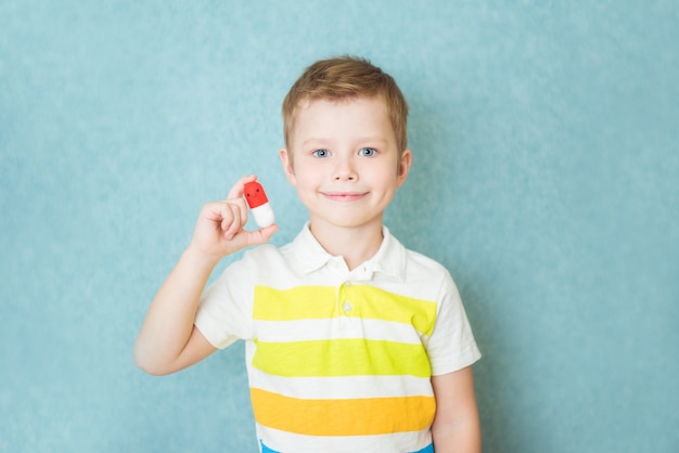 Glimlachende jongen die een capsule van vitamine op blauw houdt