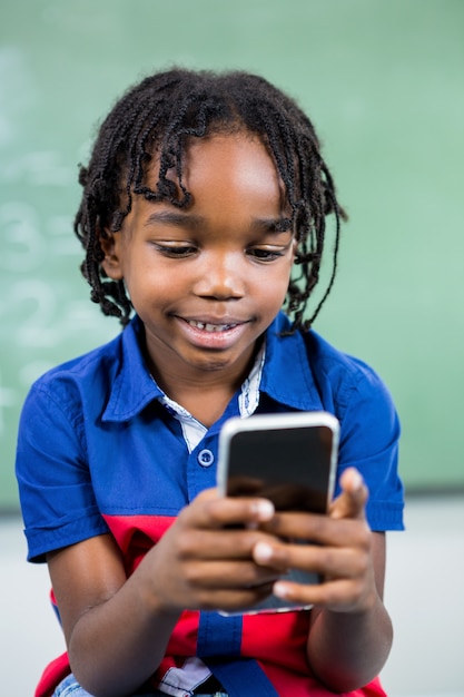 Glimlachende jongen die mobiele telefoon in klaslokaal met behulp van
