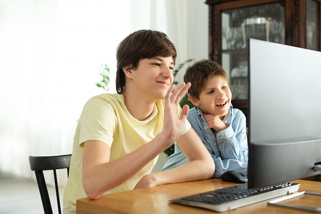 Glimlachende jongen en tiener die online babbelen en bij het computerscherm golven. Quarantaine en zelfisolatie door coronavirus.