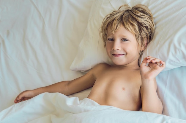 Glimlachende jongen in bed die wakker wordt in zijn bed