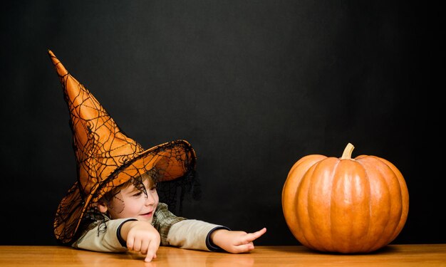 Glimlachende jongen in heksenhoed wijzend op halloween pompoen jongen toont vinger op pompoen trick or treat