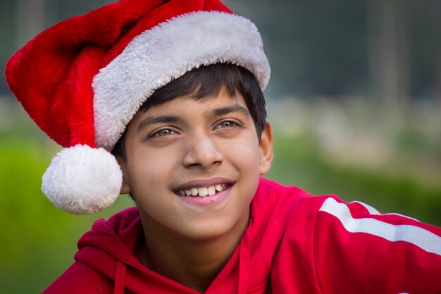 Glimlachende jongen met kerstmuts en rood t-shirt die vrolijk op afstand kijkt