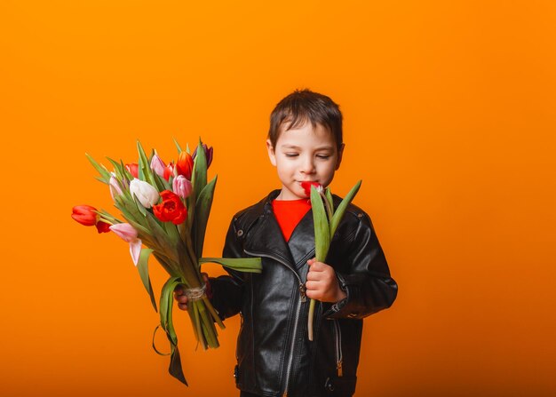 Glimlachende jongen met lentebloemboeket van tulpen geïsoleerd op geel Kleine jongen met tulpen