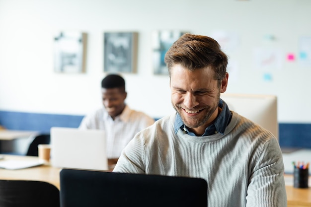 Glimlachende Kaukasische medio volwassen zakenman die aan laptop in creatief bureau werkt