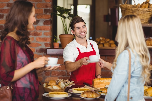 Glimlachende kelner die een koffie dient aan een klant