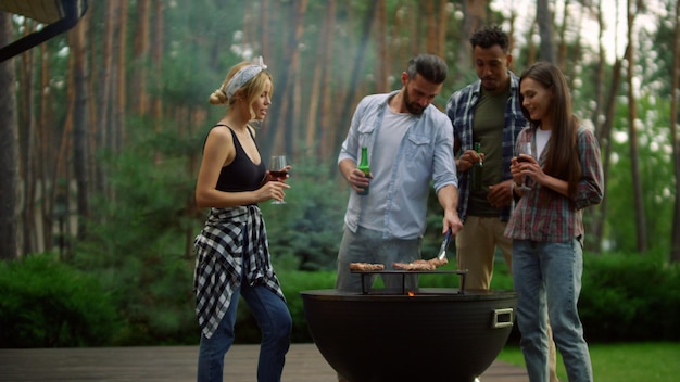 Glimlachende kerels die buiten alcoholische dranken drinken Vrienden die dichtbij bbq grill ontspannen