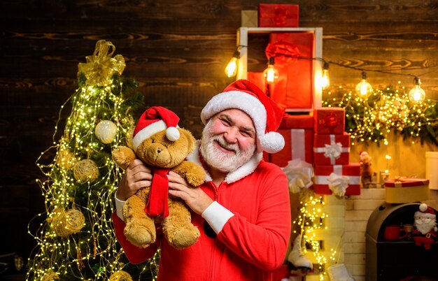 Glimlachende kerstman houdt teddybeer vast De kerstman houdt pluche speelgoedkerstversiering vrolijk