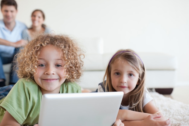 Glimlachende kinderen die een tabletcomputer met behulp van terwijl hun gelukkige ouders letten op