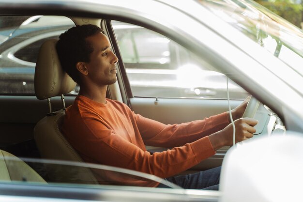 Glimlachende knappe Afro-Amerikaanse man met stijlvolle vrijetijdskleding, zittend in een auto rijdend, kijkend naar wegvervoerconcept