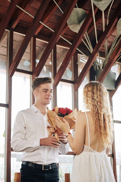 Glimlachende knappe jongeman boeket bloemen geven aan zijn vriendin