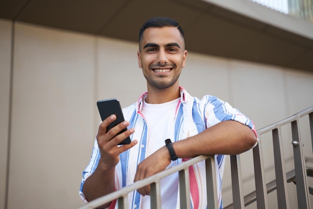 Glimlachende knappe man uit het Midden-Oosten met mobiele telefoon die online op straat winkelt