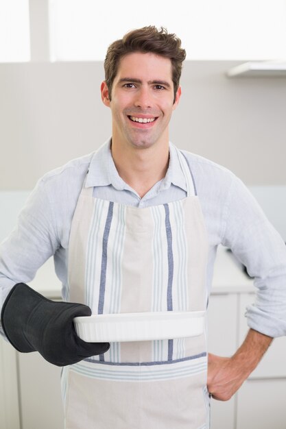 Glimlachende knappe mens die een bakselschotel in keuken houdt