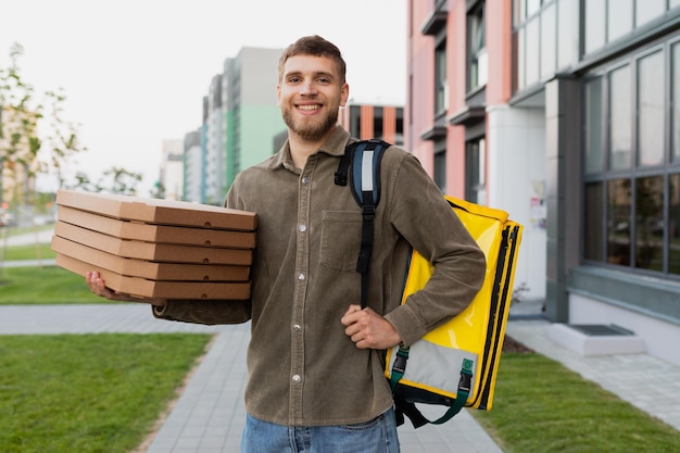 Glimlachende koeriersman met pizza in zijn handen tegen de achtergrond van het stadslandschap