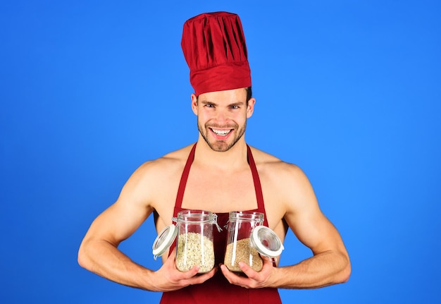 Glimlachende kok in chef-kokhoed en schort houdt glazen potten vast met korrels en granen die gezond eten koken