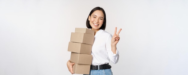 Glimlachende Koreaanse vrouw met dozen die vsign-vredesgebaar tonen die zich over witte achtergrond bevinden