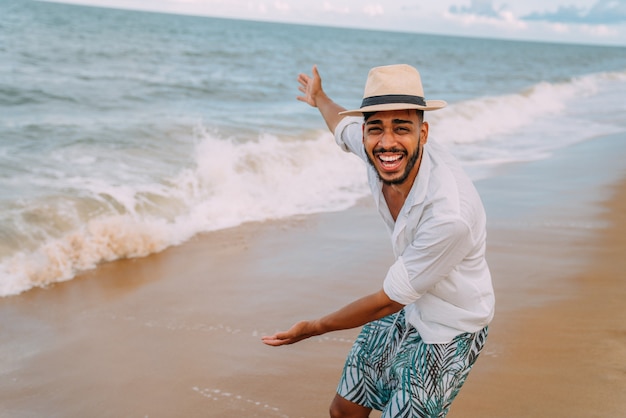 Glimlachende Latijns-Amerikaanse man op het strand gebarend naar de ruimte aan de linkerkant met zijn handpalm