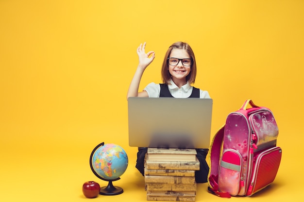 Glimlachende leerling die achter een stapel boeken zit en een laptop laat zien dat de hand zingt voor kinderen