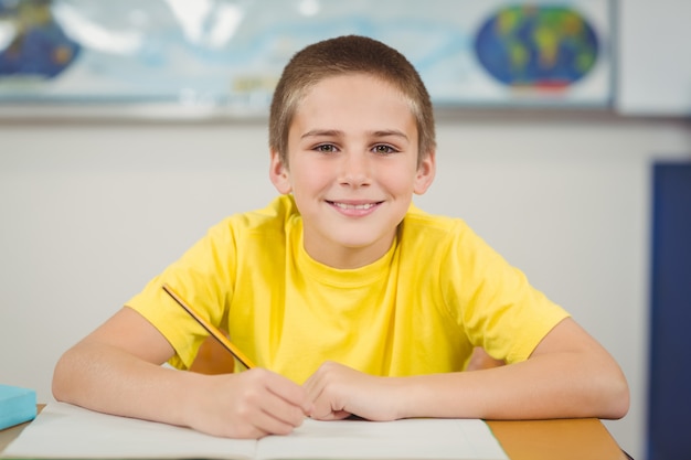 Glimlachende leerling die bij zijn bureau in een klaslokaal werkt