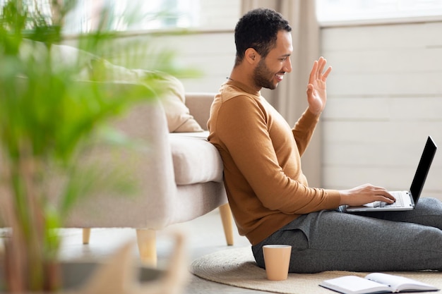 Glimlachende man aan het werk op laptop zwaaiende hand