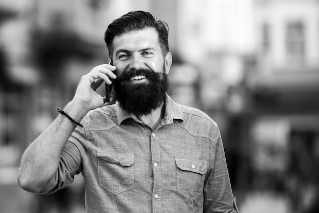 Glimlachende man bel telefoon en glimlach buiten stad straat Gelukkig zakenman in casual blauw shirt praten op mobiel