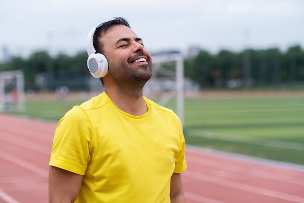 Glimlachende man die naar zijn favoriete motiverende liedje luistert via een draadloze koptelefoon die buiten traint