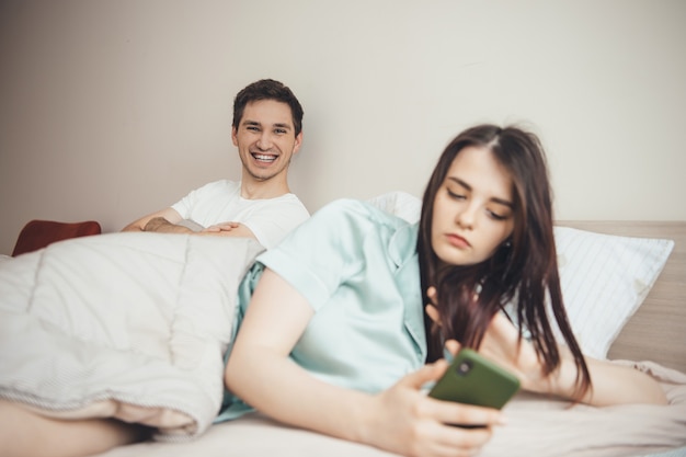 Glimlachende man die op zijn vrouw wacht om een bericht op telefoon in bed te schrijven
