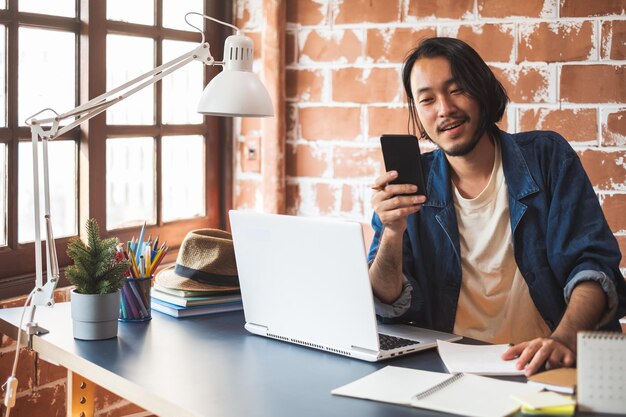 Foto glimlachende man die telefoon gebruikt met laptop op tafel op kantoor