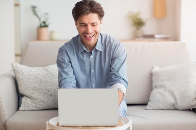 Glimlachende man die videogesprek voert via laptop zittend op de bank