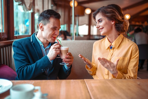 Glimlachende man drinkt een cocktail uit de rietjes tegen gelukkige vrouw in restaurant. hou van paar op romantische date