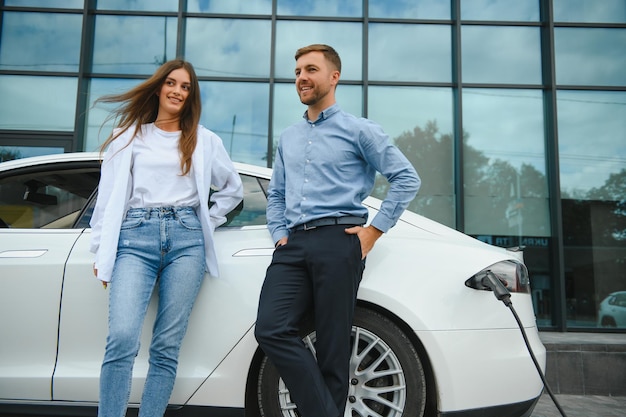 Glimlachende man en vrouw op het laadstation voor elektrische auto's Een man laadt een auto op