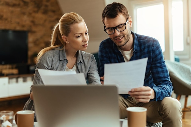 Glimlachende man en zijn vrouw analyseren hun financiële rekeningen en betalen ze thuis online