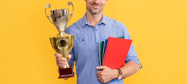 Glimlachende man houdt kampioensbeker en notitieboekje op gele achtergrondprijs?