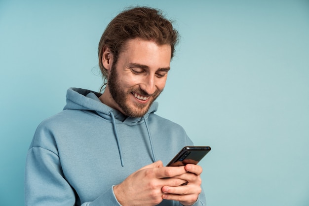 Glimlachende man met baard, in een comfortabel sweatshirt met capuchon, met een telefoon in zijn handen.