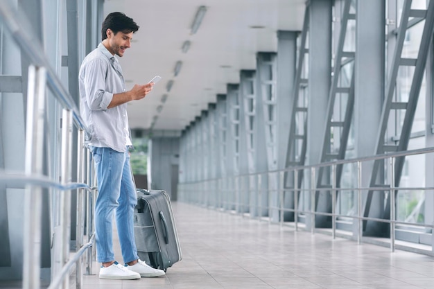 Glimlachende man met bagageberichten op zijn mobiele telefoon op de luchthaven