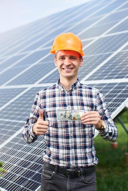 Glimlachende man met honderd dollar biljet in de hand toont duim een teken zoals op de achtergrond van zonnestation