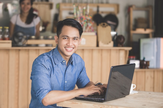 Glimlachende man met laptop in het café