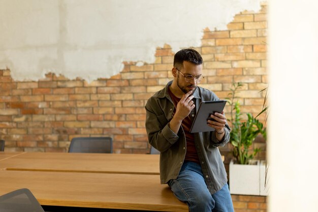 Foto glimlachende man met tablet in een modern met bakstenen ommuurd kantoor