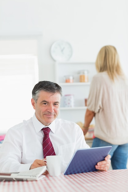 Glimlachende man met tablet pc en koffie aan de keukentafel