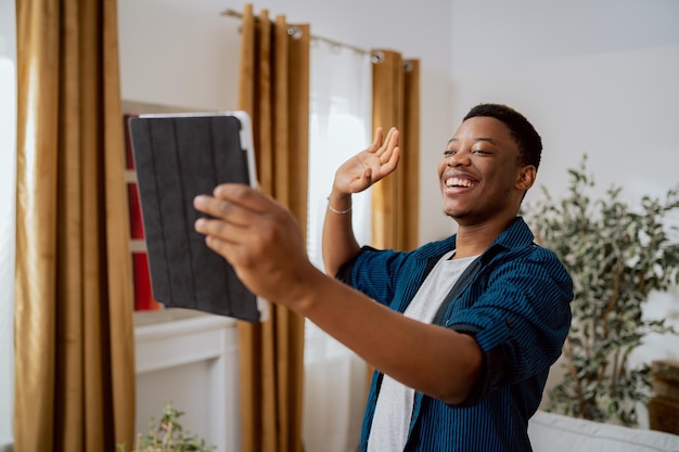 Glimlachende man ontspant na verhuizing naar nieuw appartement belt familie online, ze praten via tablet