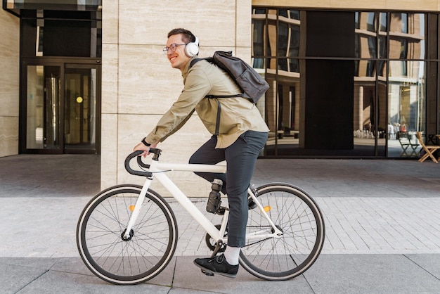 Glimlachende man op een stijlvolle witte fiets voor een modern gebouw met koptelefoon
