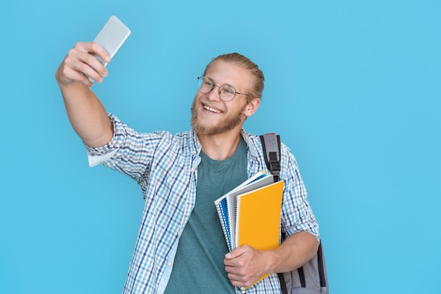 Glimlachende man student blogger houdt telefoonrecord vlog geïsoleerd op blauwe achtergrond