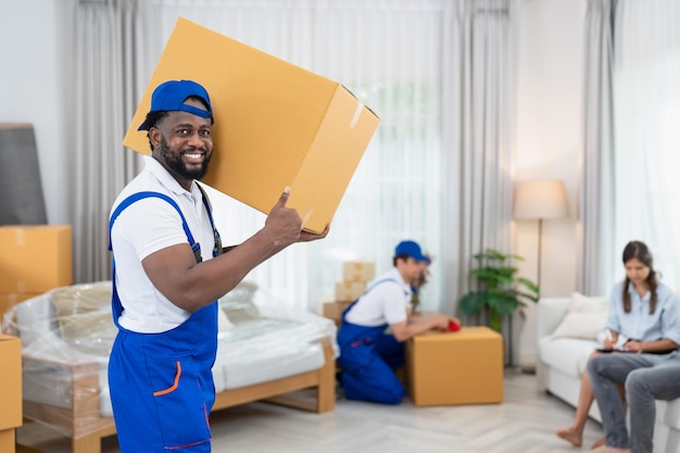 Glimlachende man verhuizer in blauw uniform met kartonnen dozen die naar de woonkamer in een nieuw huis verhuizen